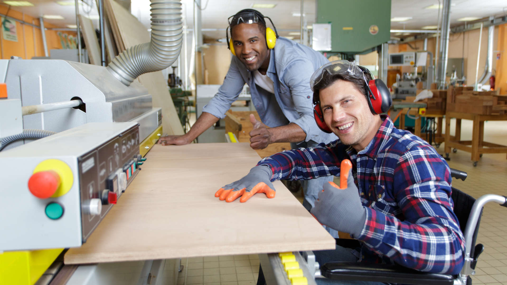 Ein Mann im Rollstuhl und ein weiterer Mann arbeiten gemeinsam an einer Holzbearbeitungsmaschine.