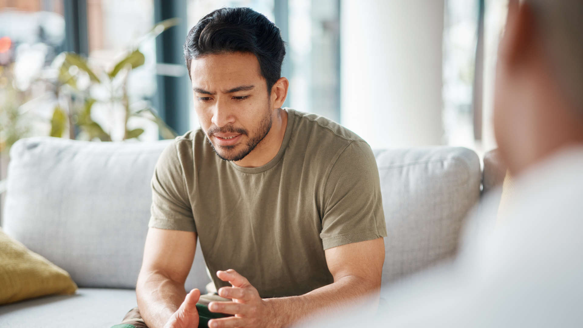 in Mann sitzt nach vorne gebeugt auf einem Sofa und gestikuliert während eines Gesprächs.