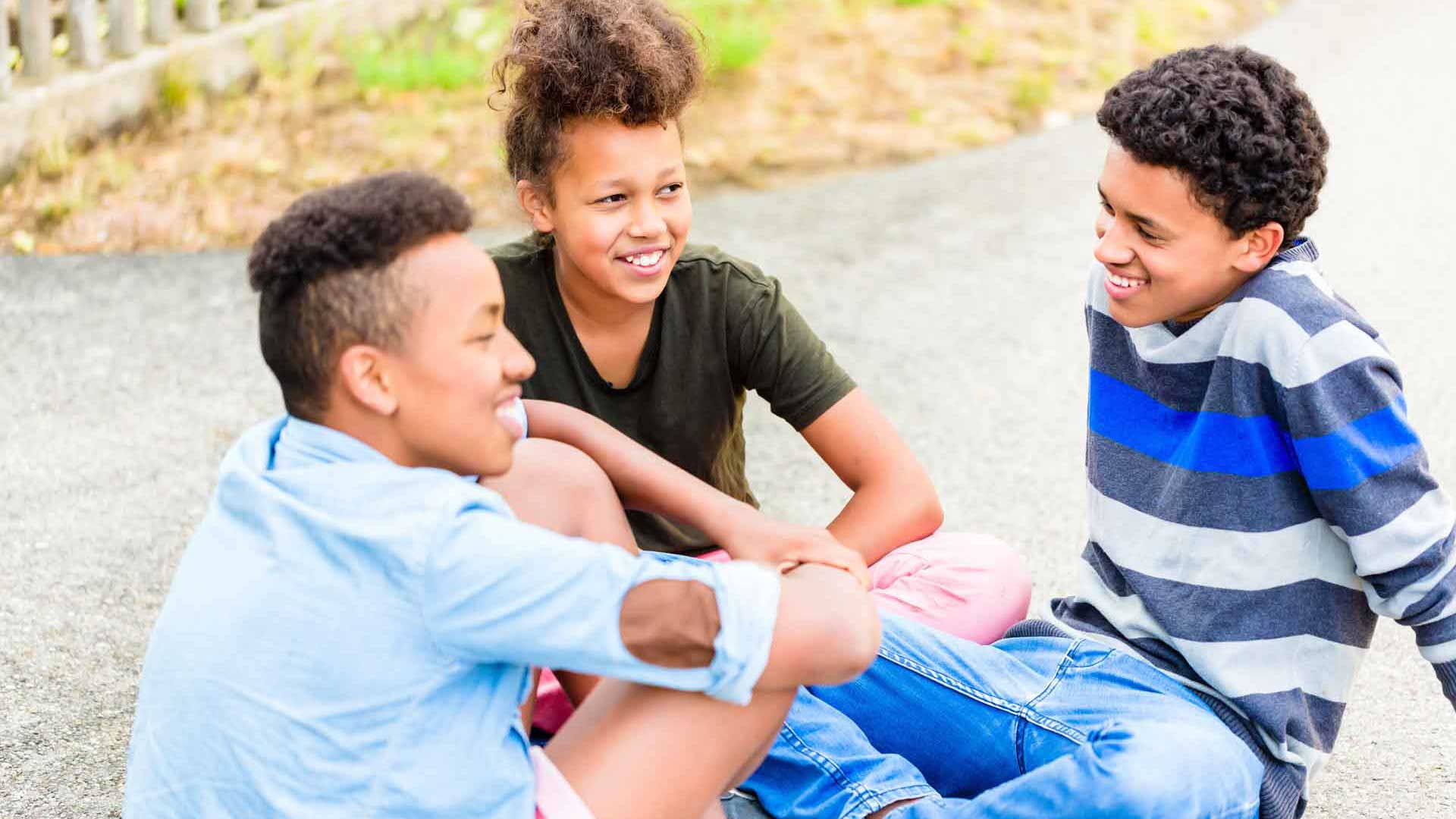 Drei Jugendliche sitzen draußen zusammen und unterhalten sich.